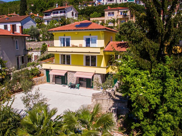 Un edificio giallo a due piani con tetto in tegole rosse, facciata in pietra e un piccolo spazio esterno con tavoli e sedie.