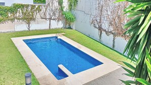A rectangular swimming pool with a concrete edge, surrounded by a well-maintained lawn and a white wall with climbing plants. - El Grullo, with community pool. (Conil de la Fra.)