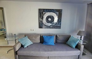 A living room with a grey sofa, two side tables, and a modern abstract painting on the wall.