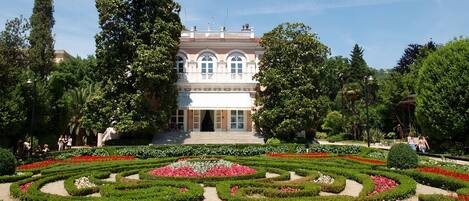A large building with a symmetrical facade, surrounded by well-manicured gardens with geometric patterns and a variety of flowering plants.