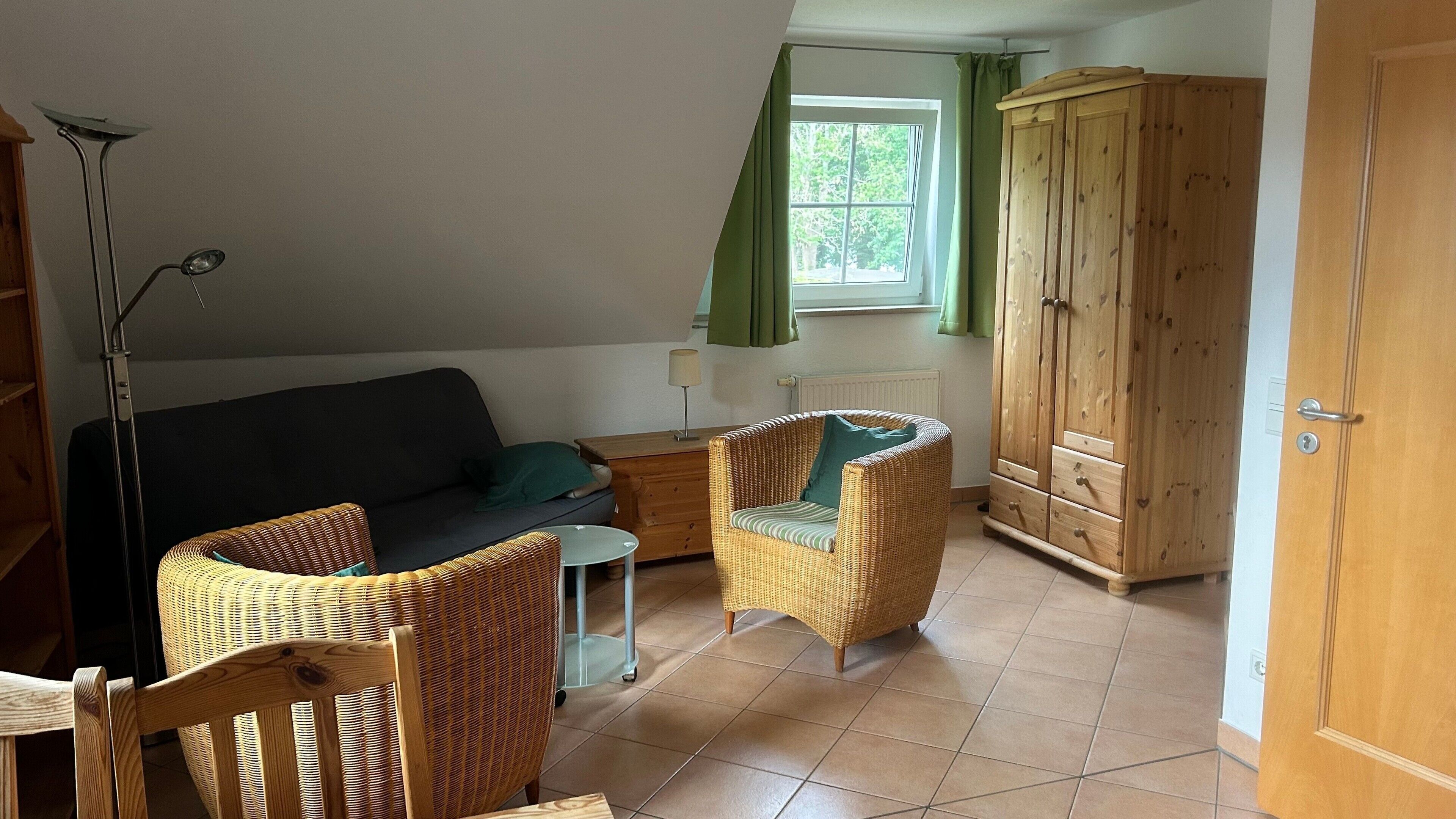 Ein Zimmer mit einer Couch, zwei Korbstühlen, einem Schrank und einer Stehlampe.