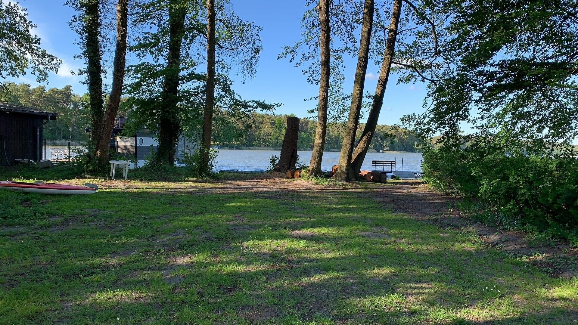 Een gebied aan een meer met bomen, een bankje en een kano.