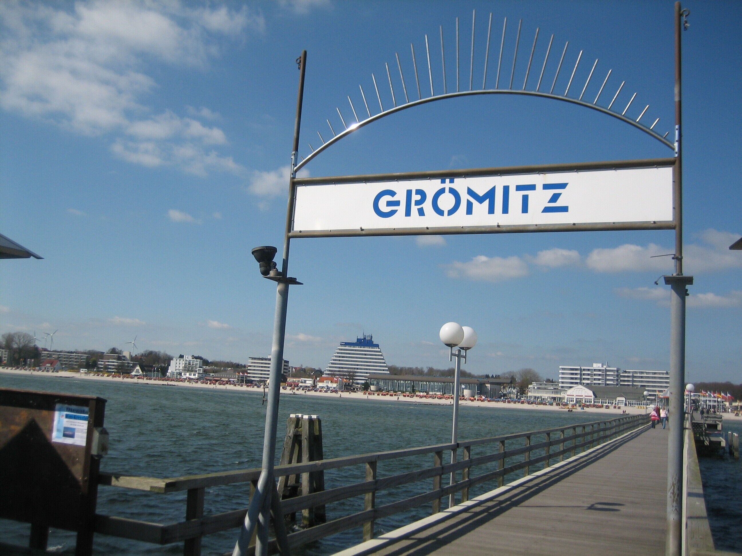 Un muelle con un letrero que dice 'GRÖMITZ' y vistas del agua y edificios al fondo.