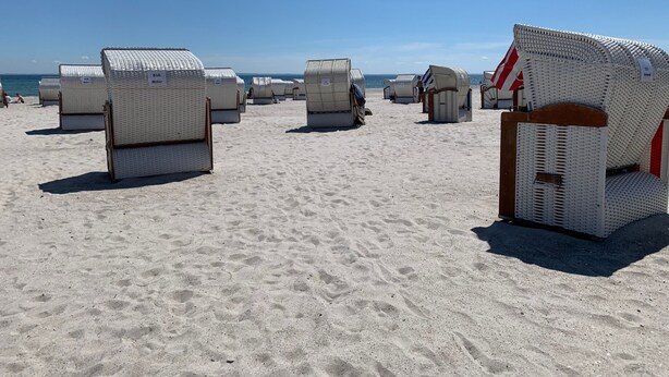 Strandstoelen staan op een zandstrand, met een heldere lucht.