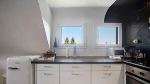 A kitchen with white cabinets, a microwave, a stove, and two windows with a view of trees. - Apartment 'Zipfelmütze' with Shared Garden, Balcony, Sauna and Wi-Fi (Feldberg)