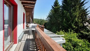 A wooden deck with a railing, a glass door, and a view of trees and hills. - Apartment 'Zipfelmütze' with Shared Garden, Balcony, Sauna and Wi-Fi (Feldberg)