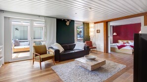 Ein modernes Wohnzimmer mit Sofa, Sessel und Couchtisch, großen Fenstern und einer roten Akzentwand.