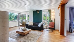 Ein modernes Wohnzimmer mit einer Couch, Sesseln, einem Couchtisch und Blick ins Freie.