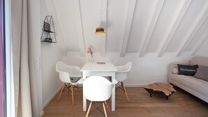 Un espace repas moderne avec une table et des chaises blanches, une table basse en bois et un luminaire suspendu.