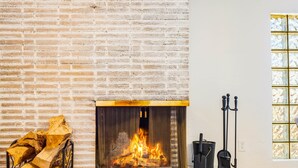 A fireplace with a fire, a stack of firewood, and a window with decorative glass. - Retreat w/ HotTub, Steam Room, BBQ, Arcade, Nintendo Switch, WorkSpace & W/D
 (Albuquerque)