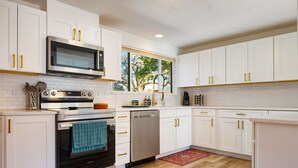 A modern kitchen with white cabinets, stainless steel appliances, and a wooden floor. - Retreat w/ HotTub, Steam Room, BBQ, Arcade, Nintendo Switch, WorkSpace & W/D
 (Albuquerque)
