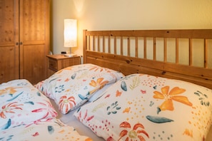 Une chambre à coucher avec une tête de lit en bois, une literie à motifs floraux, une table de chevet avec une lampe et une armoire en bois.