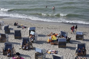 Une plage bordée de rangées de chaises de plage et de parasols à rayures, dont certaines sont occupées par des personnes.