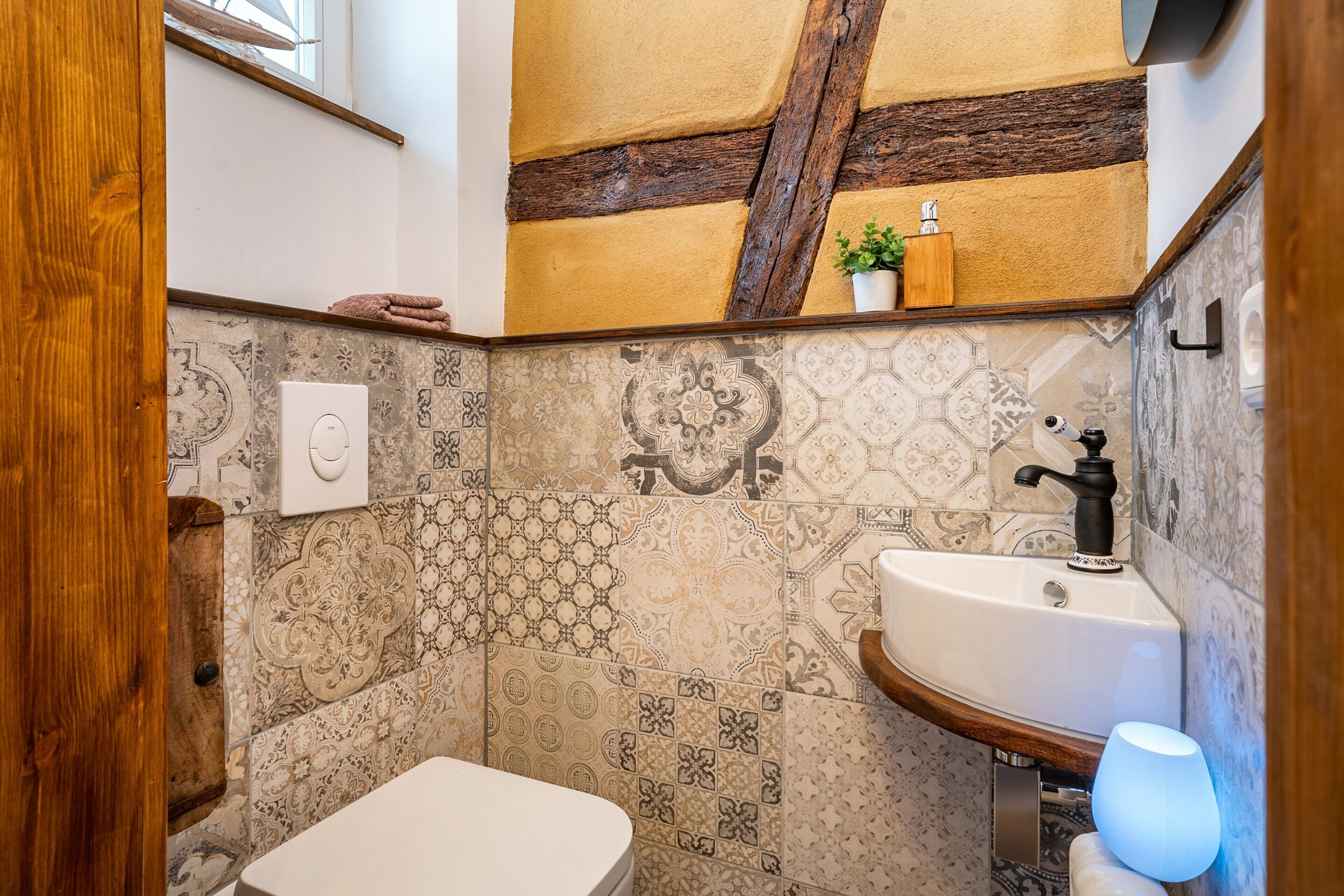 A bathroom with a white toilet, a sink with a black faucet, and a wall with patterned tiles.