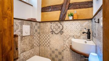 A bathroom with a white toilet, a sink with a black faucet, and a wall with patterned tiles.