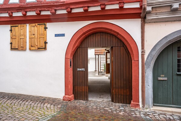 Une entrée en arc surmontée d’une porte en bois, et une porte verte sur la droite.