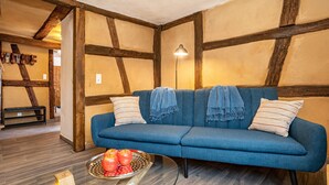 A blue sofa with striped pillows, a wooden floor, and a lamp in a room with exposed wooden beams and a wall-mounted sign. - Half-Timbered Apartment 'Fachwerk' with Wi-Fi (Neustadt an der Weinstrasse)