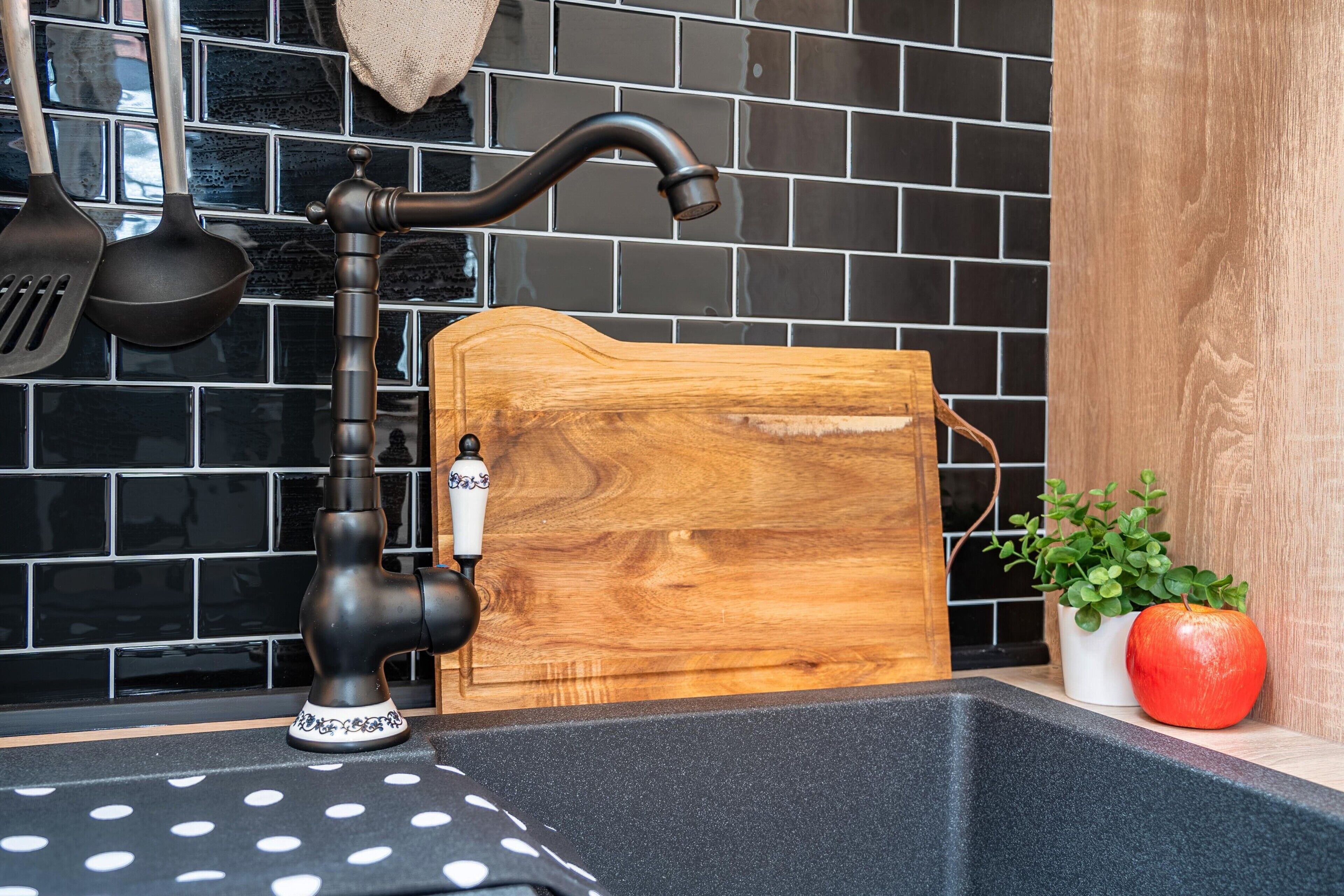 Eine Küche mit einem schwarzen Wasserhahn, einer Holz-Schneidebrett, einem Topfpflanze und einem roten Apfel.