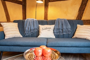 Un canapé bleu avec des coussins à rayures, un coussin blanc avec du texte et un bol de pommes posé sur le sol.