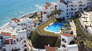 Ein Hotel an der Küste mit Pool, umgeben von weißen Gebäuden, Palmen und Blick aufs Meer.