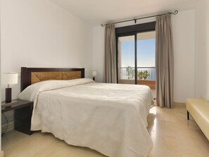 Relax in a spacious room with a large bed, bedside table, and balcony offering a view of the sea and palm trees.