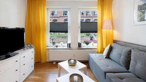 A living room with a sofa, a TV, two small tables, and a window with yellow curtains. - Characterful Apartment in the Heart of Kassel with Parking Included (Kassel)