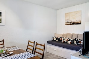 A room with a bed, a TV, a dining table with chairs, and a wall-mounted painting.