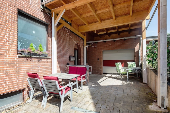 A covered patio area with brick walls, a table with chairs, and a red cushioned bench.