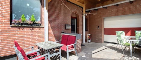 A patio area with a brick wall, a wooden table, two red cushioned chairs, and a garage door.