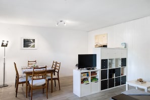 A dining area with a table and chairs, a television on a stand, and a white shelving unit with storage.