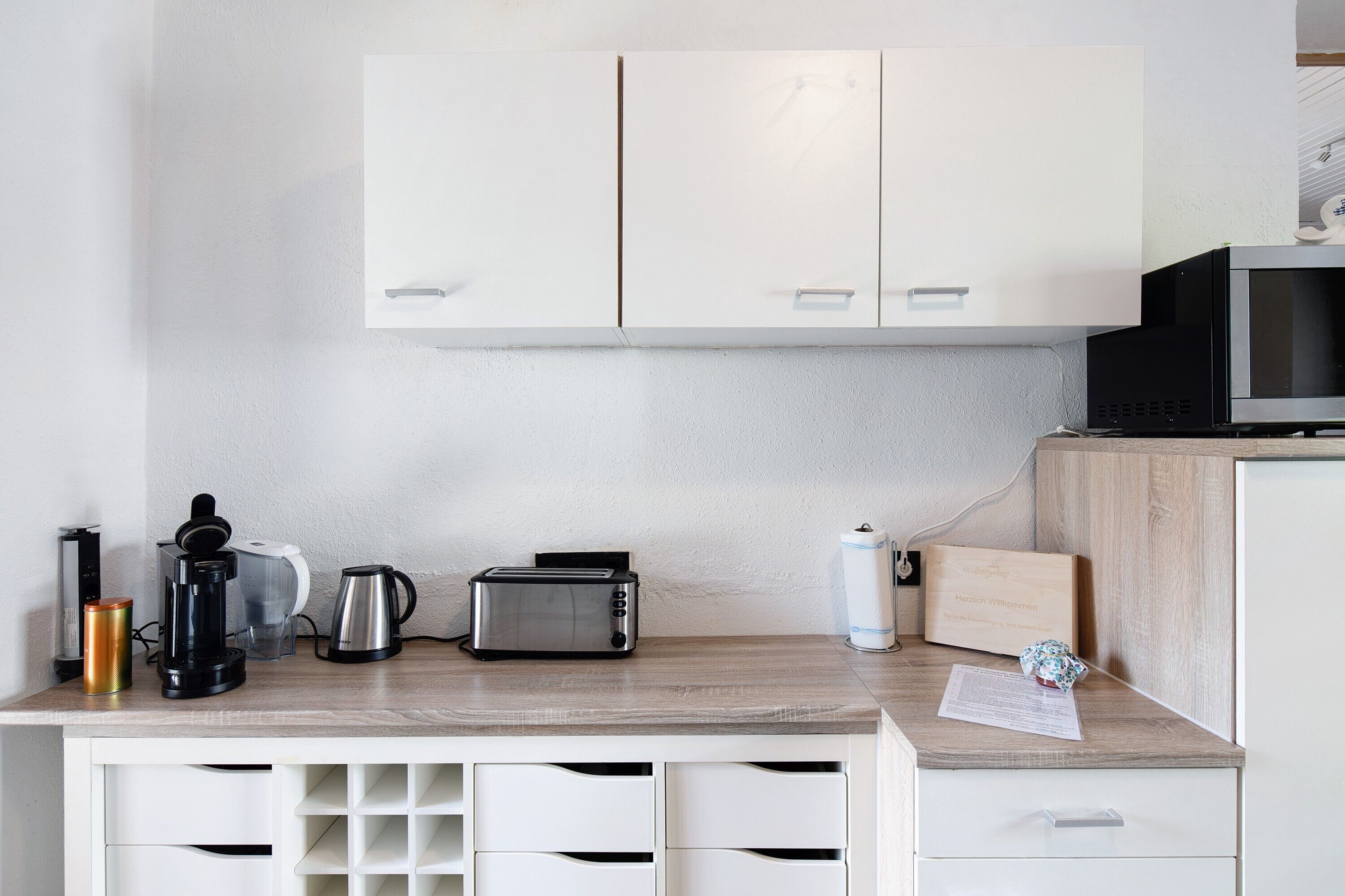 A kitchenette with white cabinets, a microwave, a toaster, a coffee maker, and a kettle.