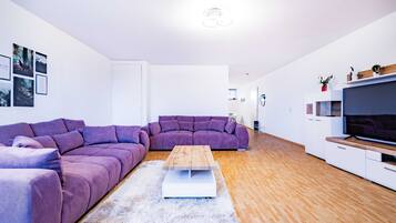Een moderne woonkamer met een paarse modulaire bank, een houten salontafel en een flatscreen televisie op een houten dressoir.