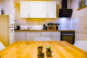 Une cuisine de taille réduite avec des meubles blancs, une table en bois et un four encastré.
