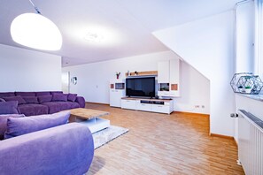 Un salon moderne avec un canapé d’angle, un téléviseur à écran plat, un plancher en bois et un escalier.