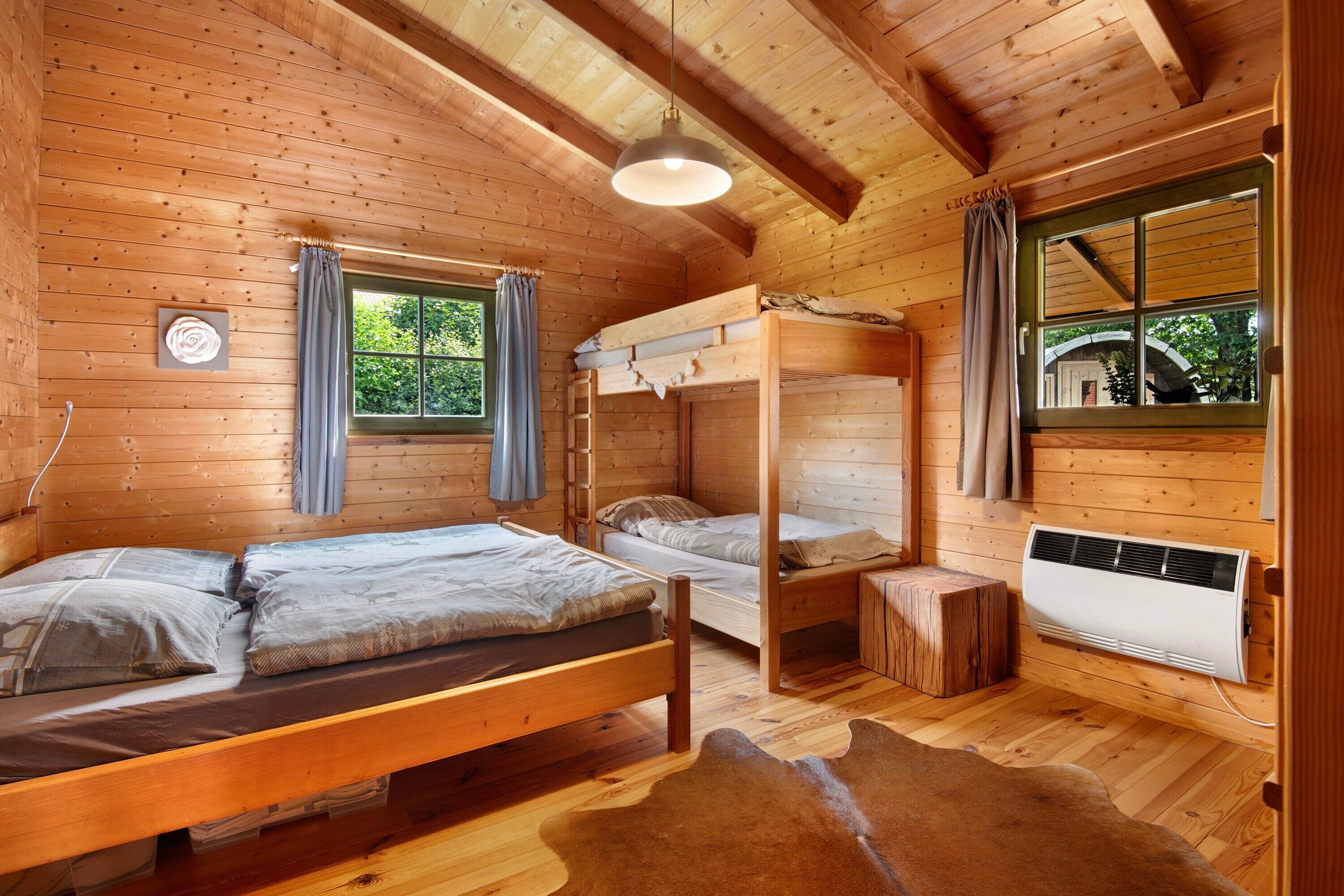 Une cabane en bois avec des lits superposés, une fenêtre avec des rideaux, un radiateur et un plancher en bois.