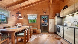 A wooden cabin interior with a dining area, kitchen, and a large window. - Chalet 'Pröllerhütte' with Private Terrace and Private Garden (St. Englmar)
