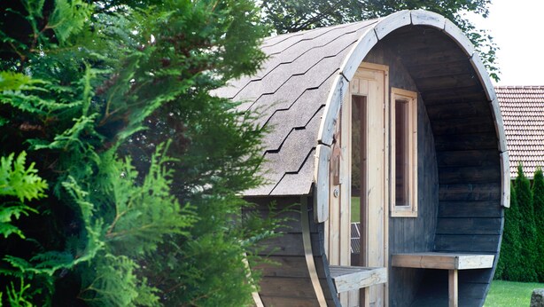 A wooden structure with a curved roof, a door, and a small porch. - Chalet 'Pröllerhütte' with Private Terrace and Private Garden (St. Englmar)