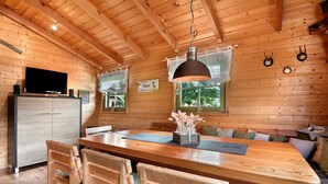 A wooden interior with a dining table, chairs, a television, and a window with a view. - Chalet 'Pröllerhütte' with Private Terrace and Private Garden (St. Englmar)