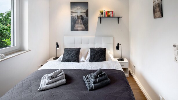 Um quarto moderno com uma cama grande, cabeceira, mesas de cabeceira, uma janela e obras de arte nas paredes.