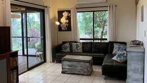 A spacious living room with a large sectional sofa, a wooden coffee table, and a sliding glass door leading to a balcony.