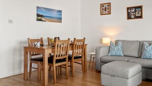 Ein Essbereich mit einem Holztisch und Stühlen, einem grauen Sofa mit gemusterten Kissen und einem kleinen Beistelltisch mit einer Lampe.