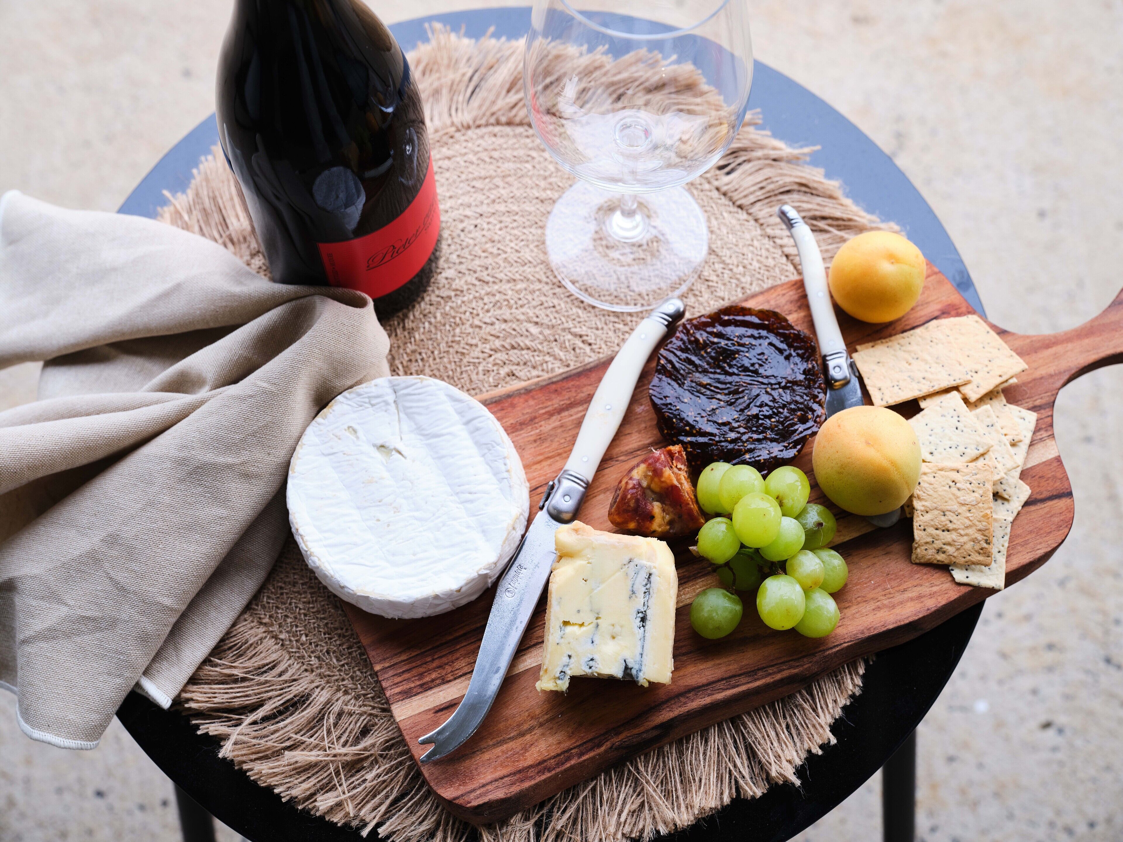 Une planche en bois sur laquelle sont disposés du fromage, des raisins, des crackers, une bouteille de vin et un couteau.