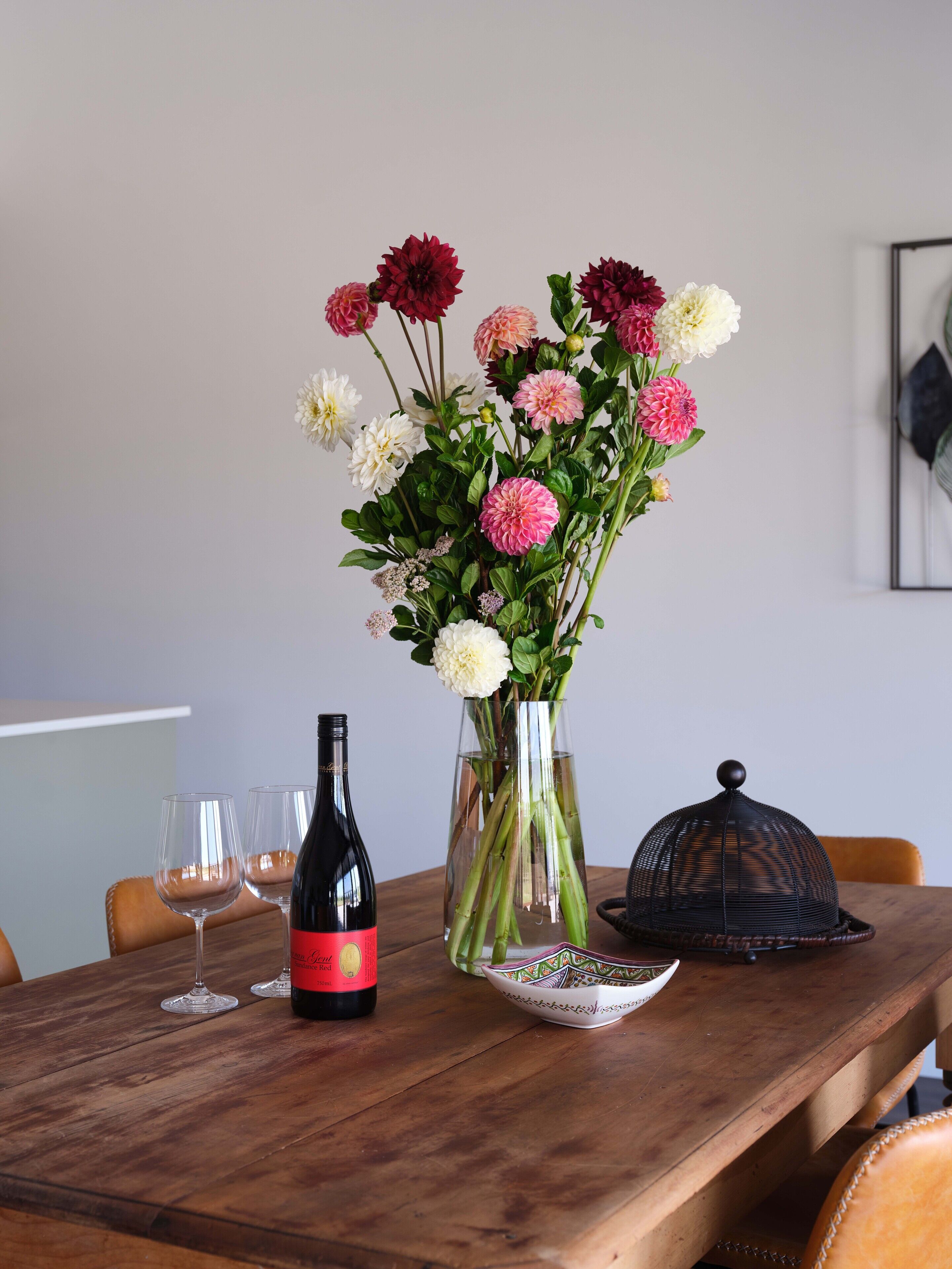 A wooden table with a vase of flowers, a wine bottle, and two glasses.