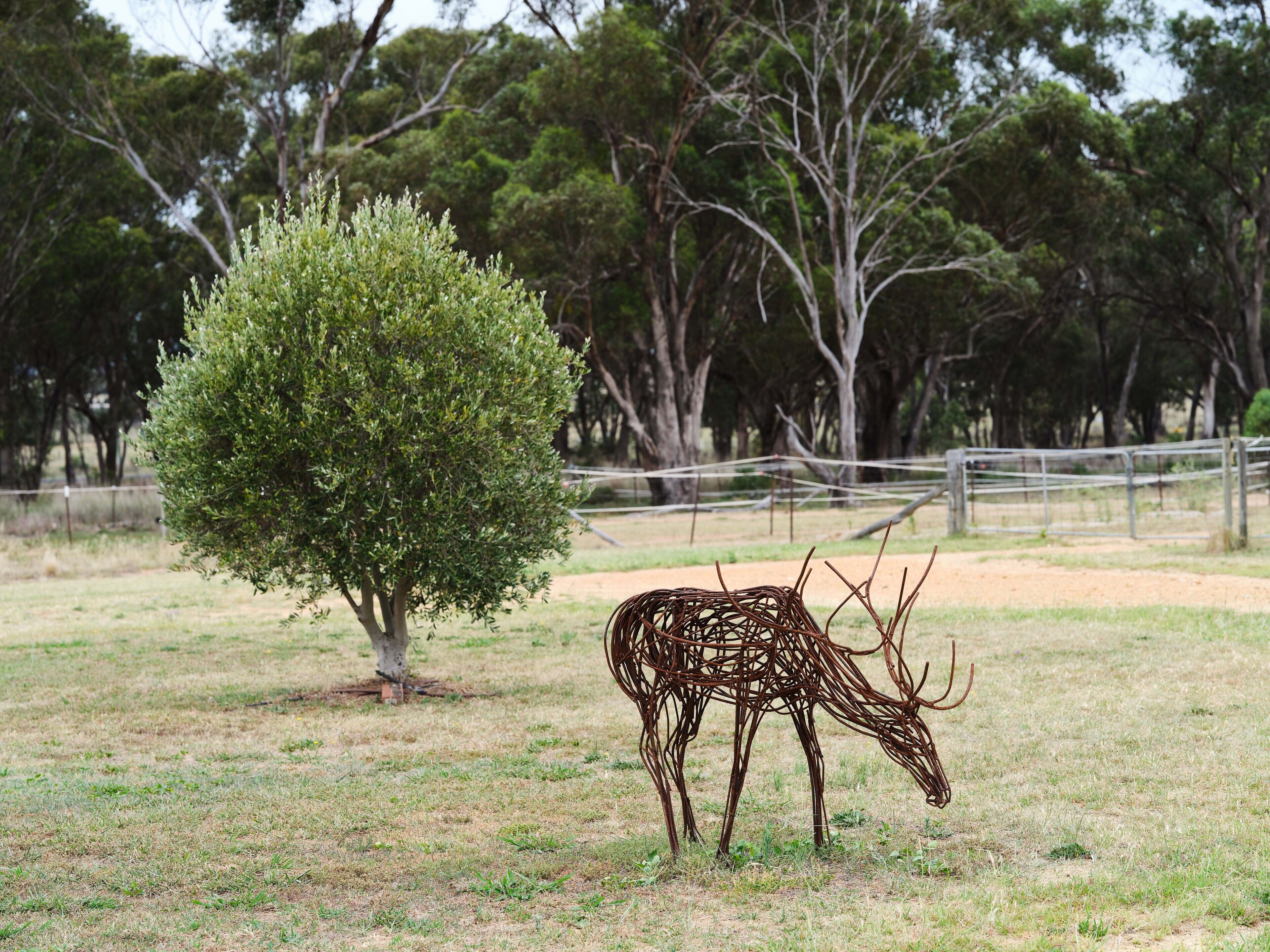 A sculpture of a deer in a grassy field with trees in the background.