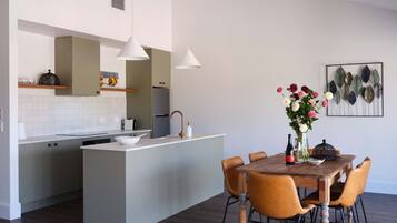 A modern kitchen with a central island, a dining area with a wooden table and chairs, and a decorative leaf wall art piece.