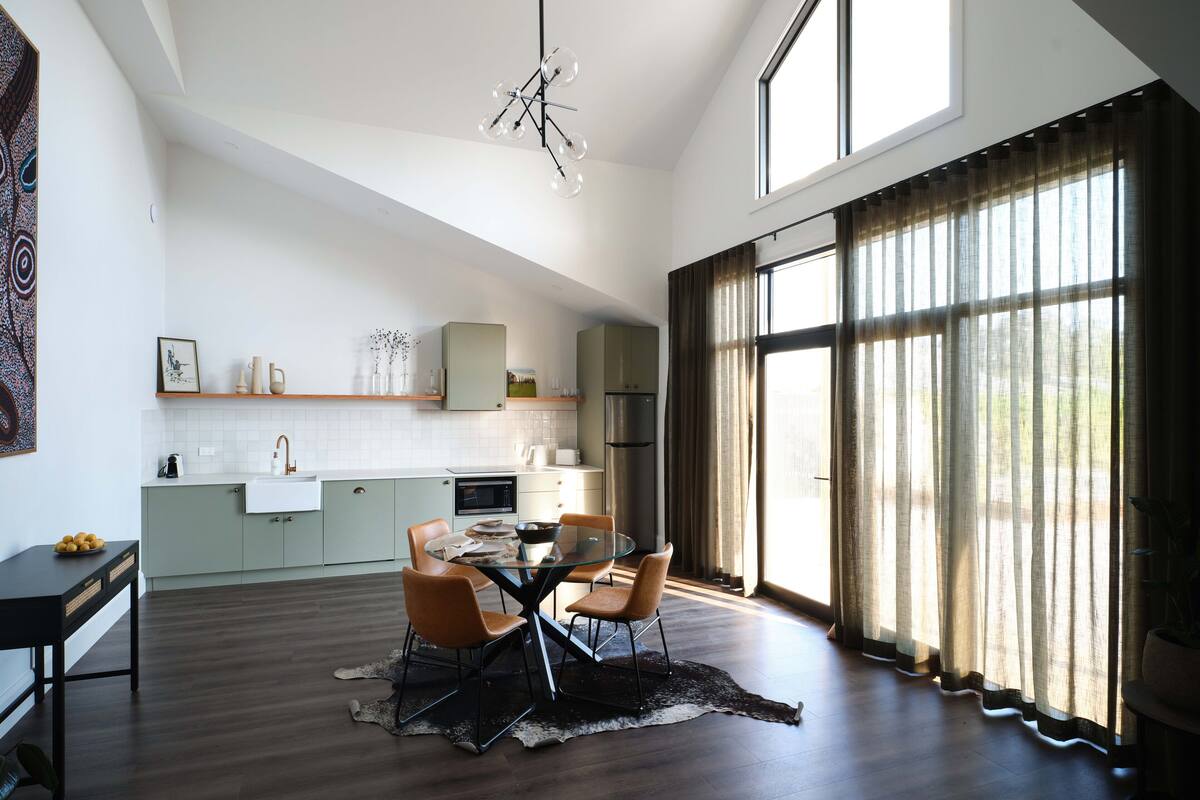 A modern kitchen with a dining area, large windows, and a unique ceiling light fixture.