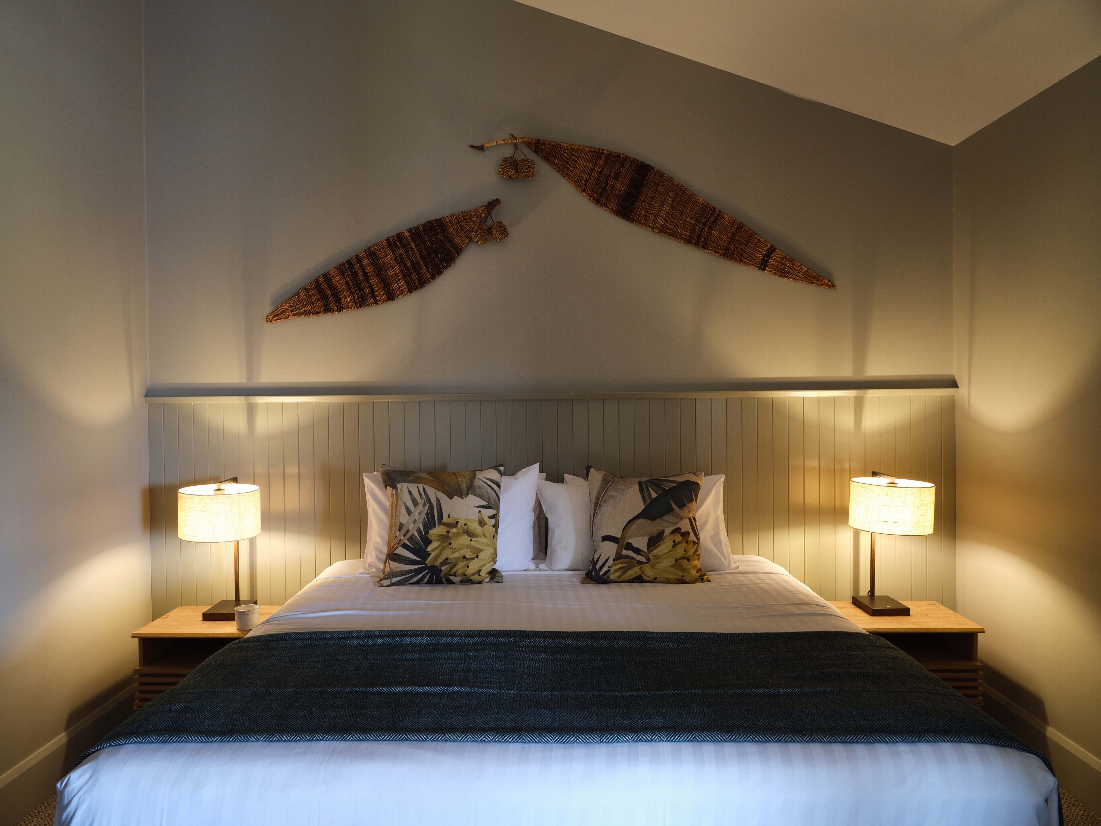 Un letto rifatto con cura, una testiera scura, due abat-jour e un elemento decorativo a parete sopra il letto.