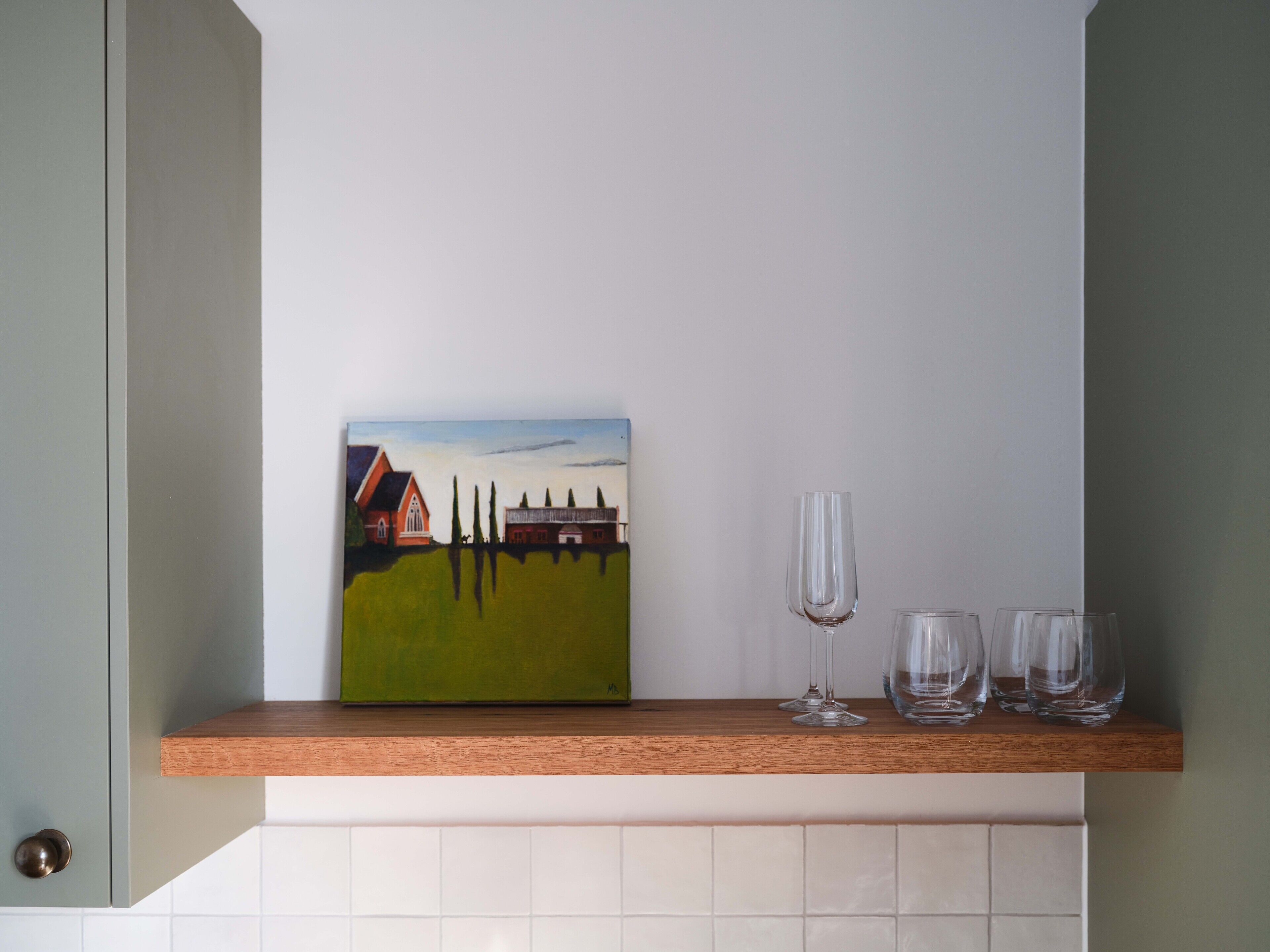 Une peinture représentant une maison posée sur une étagère, trois verres à vin et une porte.