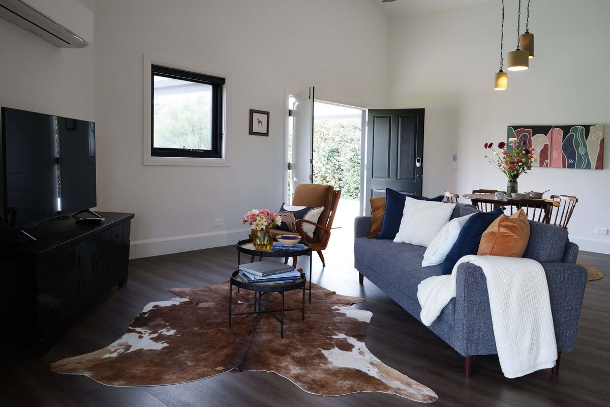 A modern living room with a flat-screen TV, a sofa, a coffee table, and a cowhide rug.