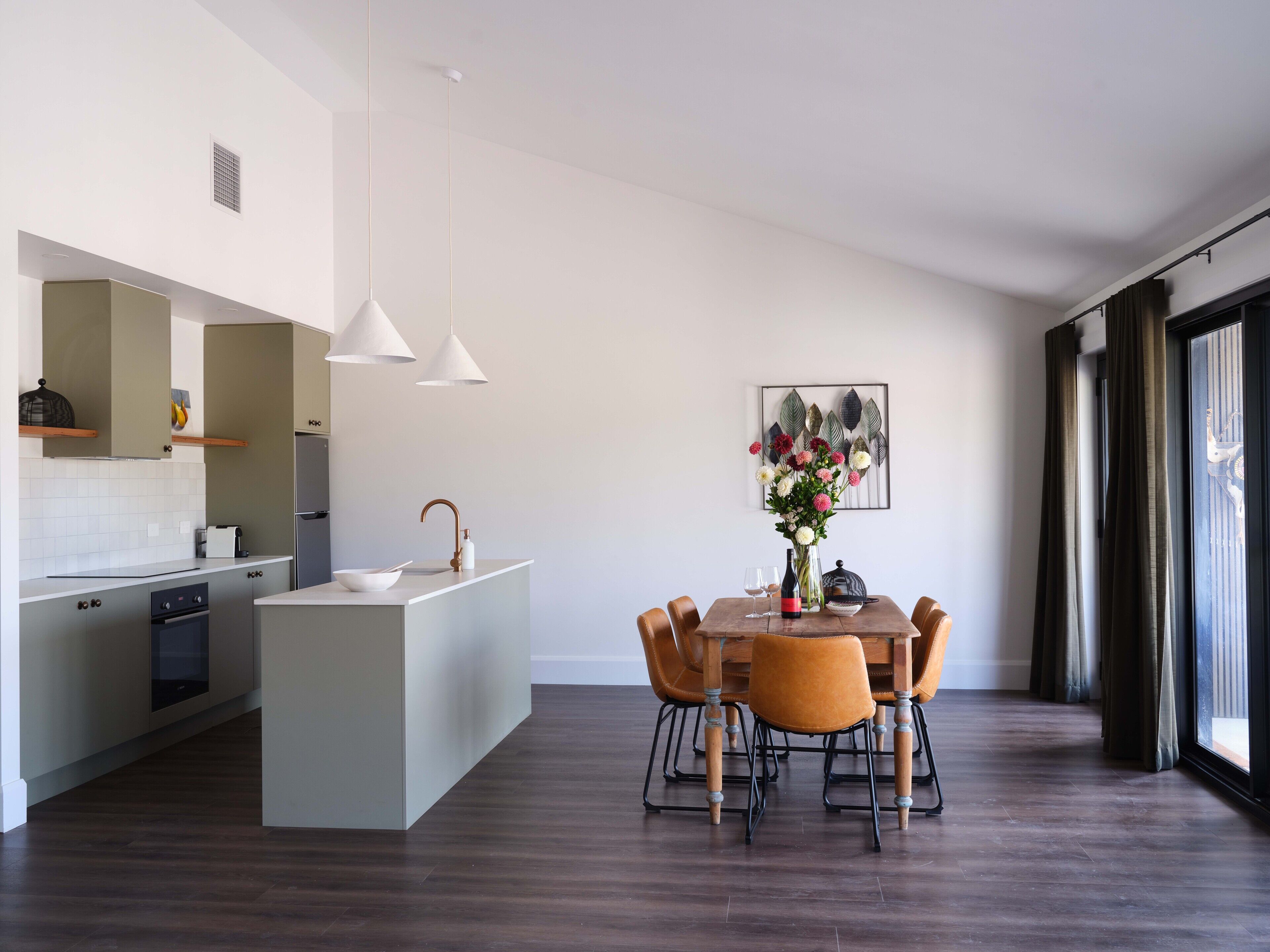 A modern kitchen with a central island, pendant lights, and a dining area with a table and chairs.